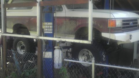 1989 Ford Bronco - A two-tone Ford Bronco is raised on a hydraulic lift, revealing its undercarriage and suspension components.