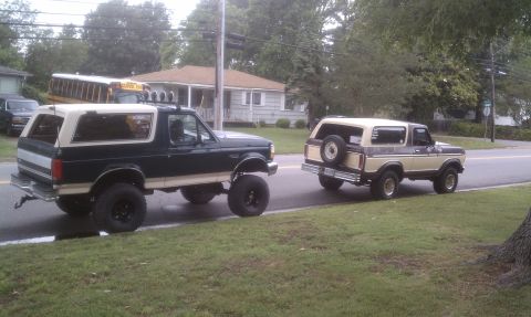 1979 Ford Bronco - Two Ford Broncos, a 1979 model and a later generation, are seen driving on a suburban street.