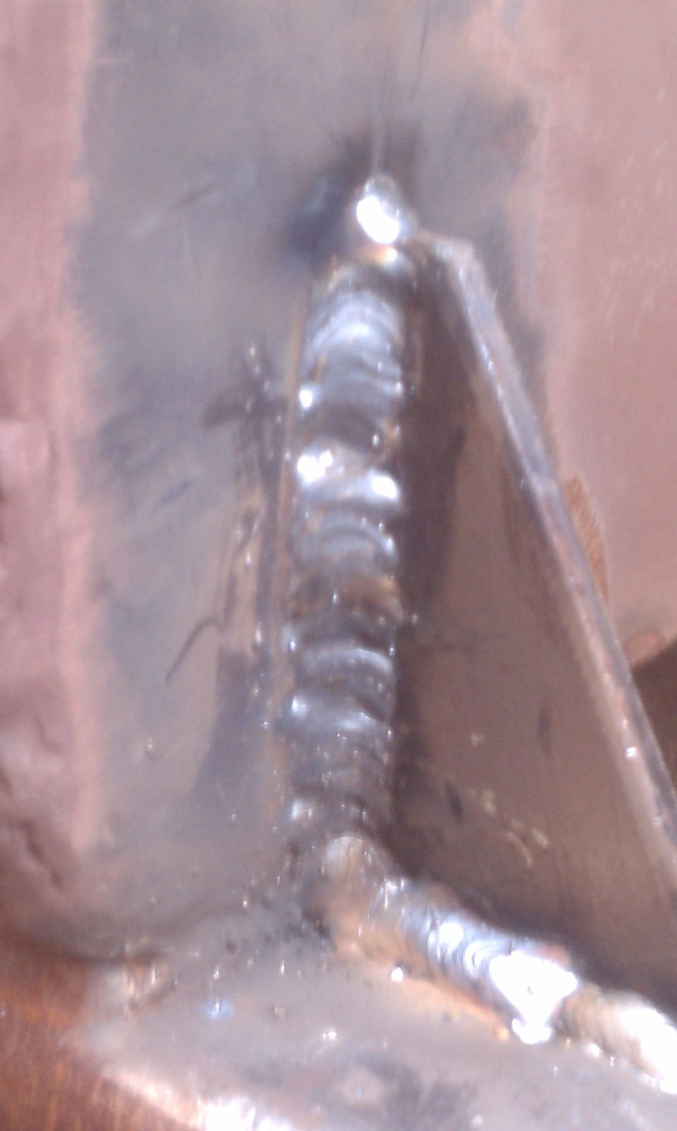 Close-up of a metal bracket with visible weld seams. Supermotors.net logo at bottom right