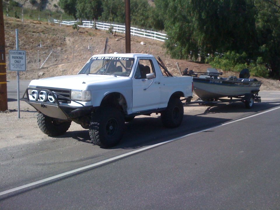 White lifted pickup truck towing an aluminum fishing boat on a roadside
