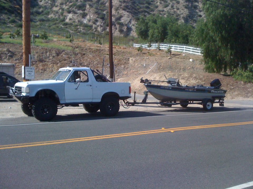 Side view of a white lifted pickup towing a Tracker fishing boat on a road