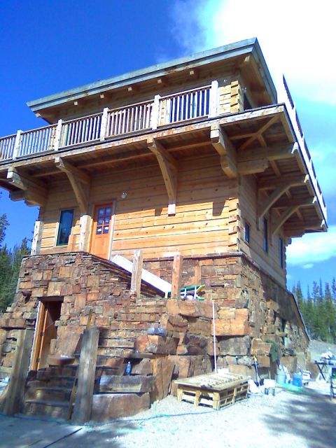 2006 Ford E350 - A rustic wooden cabin with a stone base is shown under a bright blue sky.