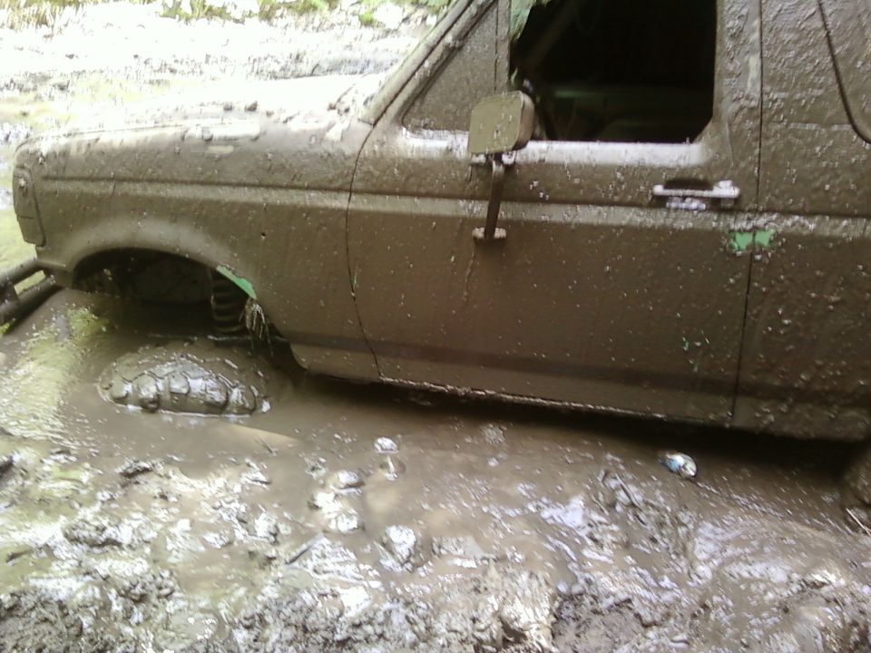 Mud-covered SUV stuck in deep brown mud, side view