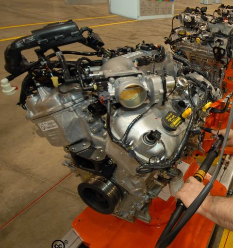 1997 Ford Taurus - An engine assembly is shown on an orange stand, various hoses, wiring, and a throttle body, likely in a manufacturing or assembly line sett…