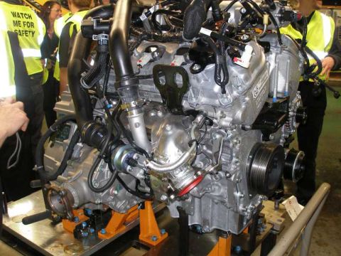 1997 Ford Taurus - Engine assembly is displayed on orange stands, with individuals in safety vests observing.