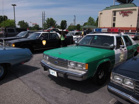 1991 Ford Crown Victoria - A police car with a light bar sits in a parking lot, with other vehicles nearby.