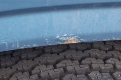 1980 Ford Bronco - A close-up view of a blue vehicle's lower body panel shows significant rust damage above a tire.
