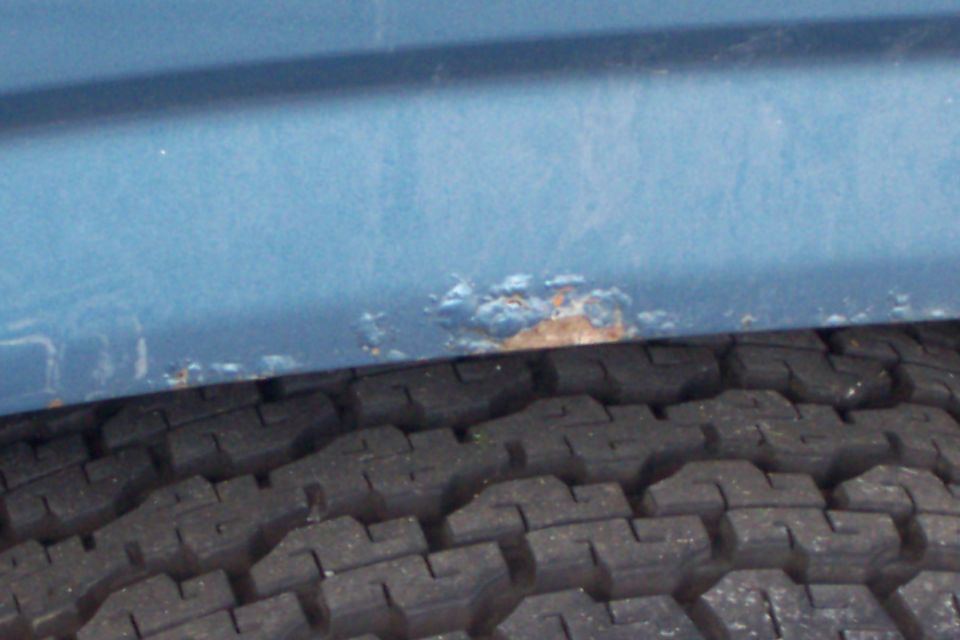 Blue vehicle body panel with rust near a tire
