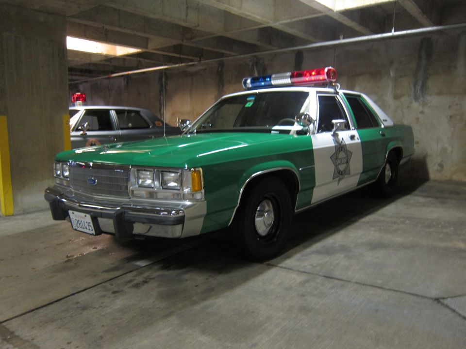 Green and white Ford police sedan with star emblem in a parking garage