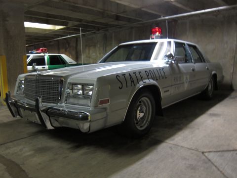 1991 Ford Crown Victoria - A silver police sedan with "STATE POLICE" markings is parked in a garage, with another police car visible behind it.