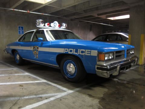 1991 Ford LTD Crown Victoria - blue-and-white Pontiac sedan lettered 'POLICE' with multiple roof beacons sits in a concrete parking garage.