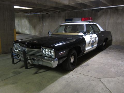 1991 Ford LTD Crown Victoria - black-and-white 1970s Dodge Highway Patrol sedan with a star door emblem and push bumper, parked in a concrete garage.