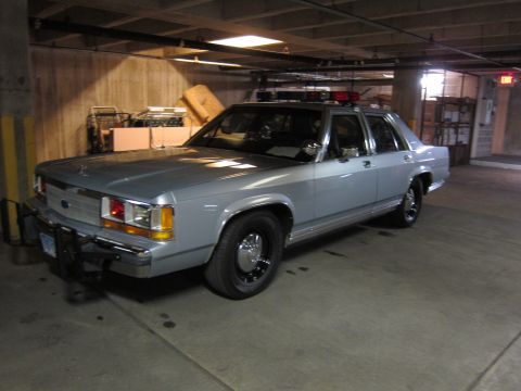 1991 Ford LTD Crown Victoria - silver Ford LTD Crown Victoria police-style sedan with a roof light bar, parked in a dim concrete garage.