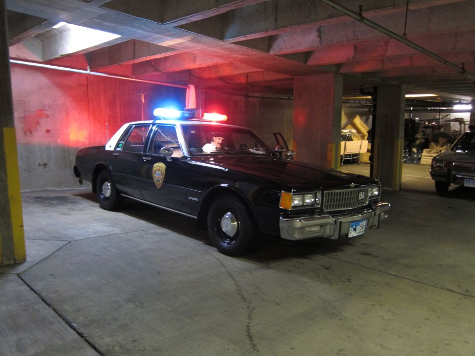 Dark Chevrolet Caprice police car with lit red roof lights in garage