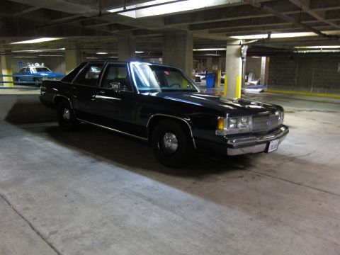 1991 Ford LTD Crown Victoria - black Ford LTD Crown Victoria police sedan with chrome trim and a red dash light, parked in a dim concrete garage.