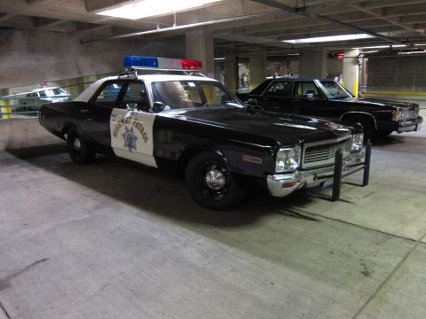 1991 Ford LTD Crown Victoria - black-and-white Highway Patrol sedan with roof lights and push bumper, parked among other patrol cars in a garage.