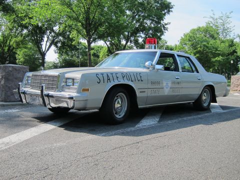 1991 Ford LTD Crown Victoria - silver 'State Police' Rhode Island sedan with a red roof beacon and chrome grille, parked outdoors on pavement.