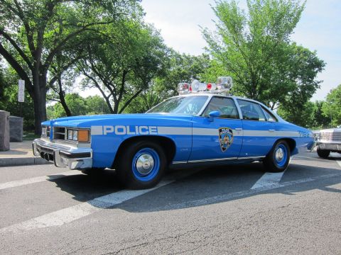 1991 Ford LTD Crown Victoria - blue Pontiac 'POLICE' NYPD sedan with white striping and roof lights, parked outdoors on a tree-lined street.