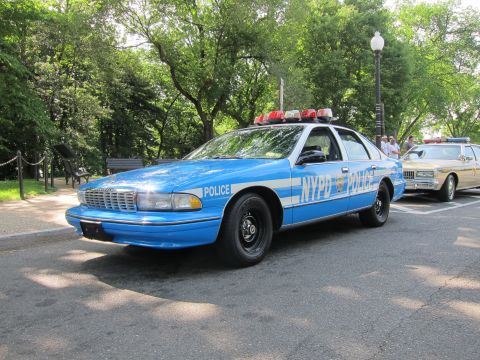 1991 Ford LTD Crown Victoria - blue-and-white Chevrolet Caprice marked 'NYPD POLICE' with red roof lights, parked outdoors among trees.
