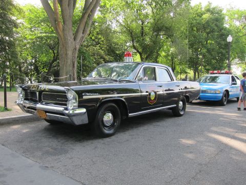1991 Ford LTD Crown Victoria - black Pontiac Catalina 'POLICE' sedan with a single red roof beacon and door shield, parked on a tree-lined street.