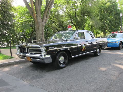 1991 Ford LTD Crown Victoria - black Pontiac Catalina 'POLICE' sedan with a gold door shield and red roof beacon, parked beside a blue patrol car.