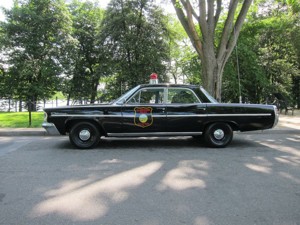 Black vintage Pontiac police sedan with red beacon, side profile outdoors