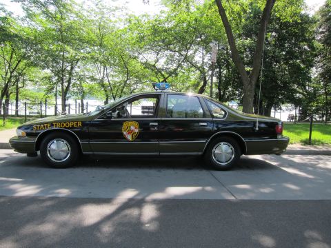1991 Ford LTD Crown Victoria - black Chevrolet Caprice marked 'STATE TROOPER' with a shield emblem and roof beacon, shown in side profile.