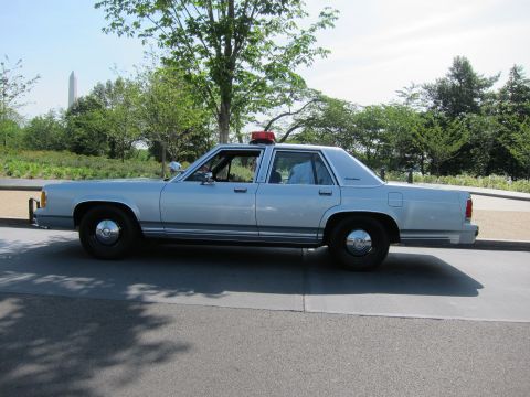 1991 Ford LTD Crown Victoria - silver Ford LTD Crown Victoria police sedan with a red roof beacon, shown in side profile with an obelisk monument behind.