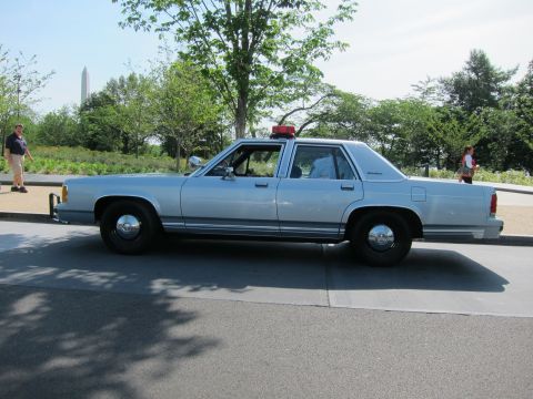 1991 Ford LTD Crown Victoria - silver 1980s Ford LTD Crown Victoria police sedan with a single red roof beacon, parked on a road with an obelisk monument in the backgroun…