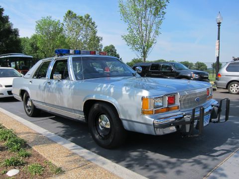 1991 Ford LTD Crown Victoria - silver Ford LTD Crown Victoria police sedan with a roof light bar and rear push bar, parked in a lot among other vehicles.