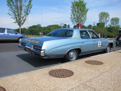1991 Ford LTD Crown Victoria - light blue early-1970s full-size police sedan lettered POLICE with a round door emblem and red roof beacon, parked beside a curb.