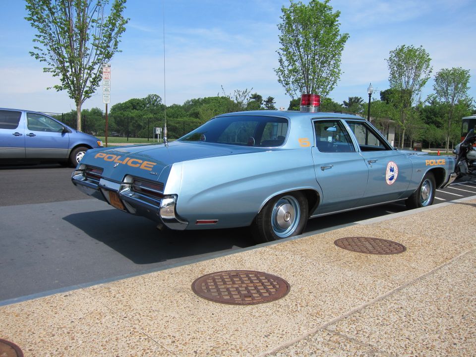 Light blue 1970s full-size police sedan marked POLICE, rear three-quarter view