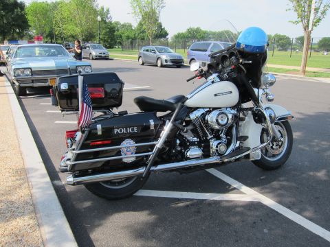 1991 Ford LTD Crown Victoria - white Harley-Davidson police motorcycle lettered POLICE, fitted with a blue helmet, saddlebags and a small US flag, parked in a lot.