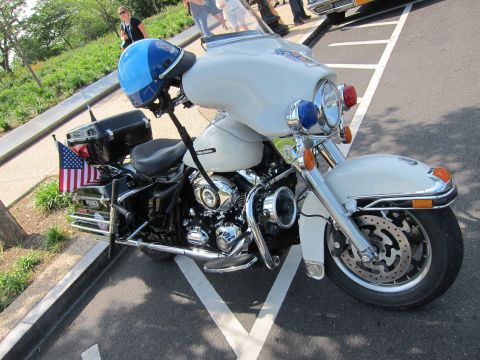 1991 Ford LTD Crown Victoria - white Harley-Davidson police motorcycle with a fairing, blue helmet on the handlebars and a small US flag, parked at a curb.