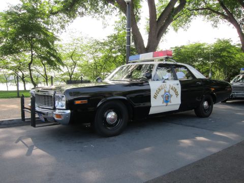 1991 Ford LTD Crown Victoria - black-and-white 1970s Dodge Highway Patrol sedan with a star emblem and red roof light bar, parked under leafy trees.