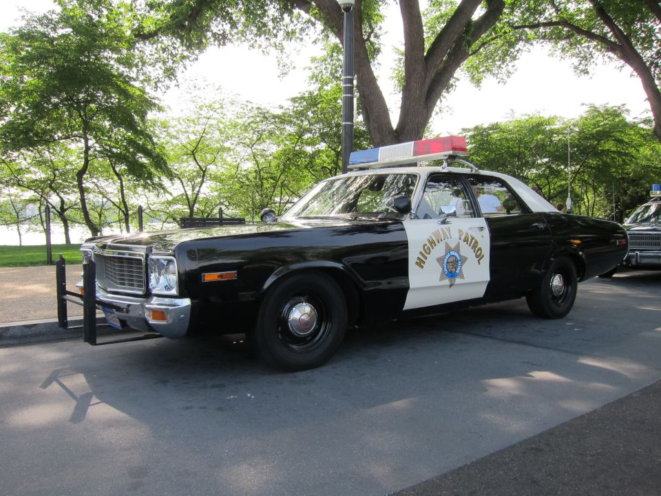 Black and white 1970s Dodge Highway Patrol sedan, front three-quarter, red light bar