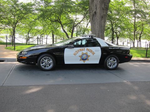1991 Ford LTD Crown Victoria - black-and-white Chevrolet Camaro Highway Patrol car with a gold star door emblem reading Safety and Service, parked along a waterfront road.