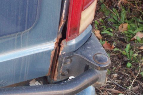 1980 Ford Bronco - Rust damage is visible on the rear quarter panel of a blue SUV, near the taillight assembly and bumper mount.