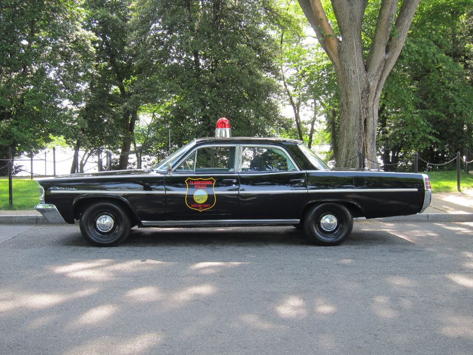 Black 1960s Pontiac Catalina police sedan with red beacon and shield, side profile