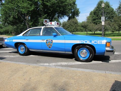 1991 Ford LTD Crown Victoria - blue-and-white 1970s Pontiac NYPD police sedan lettered POLICE with the NYPD shield and unit number 1162, shown in side profile.