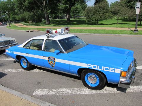 1991 Ford LTD Crown Victoria - Front-three-quarter view of a blue-and-white NYPD police sedan with roof lightbar parked in a tree-lined park.