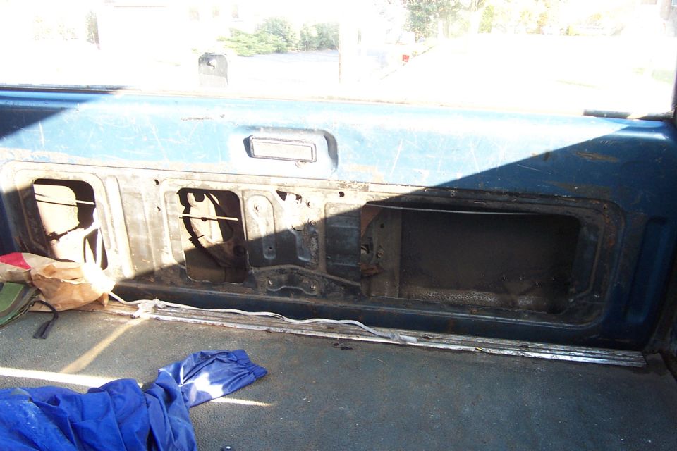 Interior view of a blue vehicle showing open storage compartments on the rear panel. Blue tarp and bag are on the floor