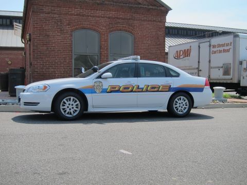 1991 Ford LTD Crown Victoria - white Chevrolet Police sedan with blue-and-orange striping parked on a street by an old brick building.