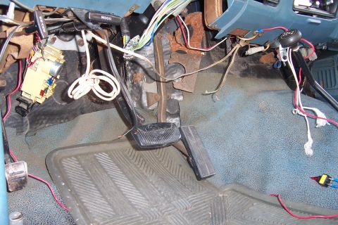 1980 Ford Bronco - The complex and exposed wiring under the dashboard of a vehicle, with pedals and floor mat visible.