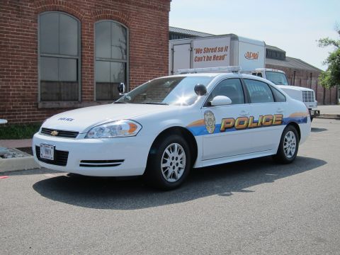 1991 Ford LTD Crown Victoria - Front-three-quarter view of a white Chevrolet Police sedan with striped graphics parked near a brick wall.