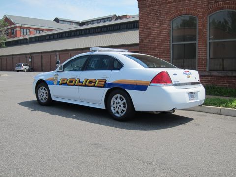 1991 Ford LTD Crown Victoria - Rear-three-quarter view of a white Chevrolet Police sedan with blue-and-orange stripes by a brick building.