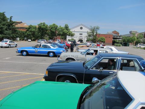 1991 Ford LTD Crown Victoria - lineup of classic police cars, including a blue and white NYPD sedan and a State Police unit, parked in a lot near a white building.