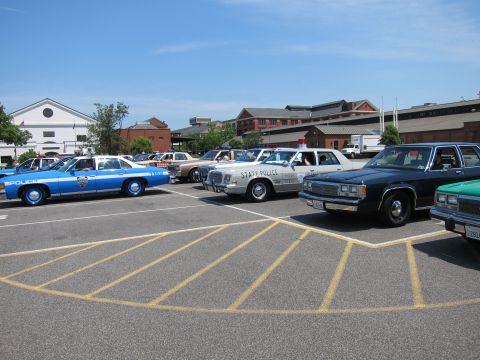 1991 Ford LTD Crown Victoria - row of vintage police sedans, a blue NYPD unit at left and a white State Police car center, parked in marked spaces.