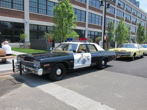 1991 Ford LTD Crown Victoria - black-and-white Highway Patrol police sedan with a star emblem and roof beacon parks on pavement near a brick loft building.