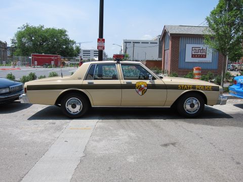 1991 Ford LTD Crown Victoria - tan-and-brown State Police sedan with a Maryland shield door emblem sits in profile at a curb near the Foundry Lofts.